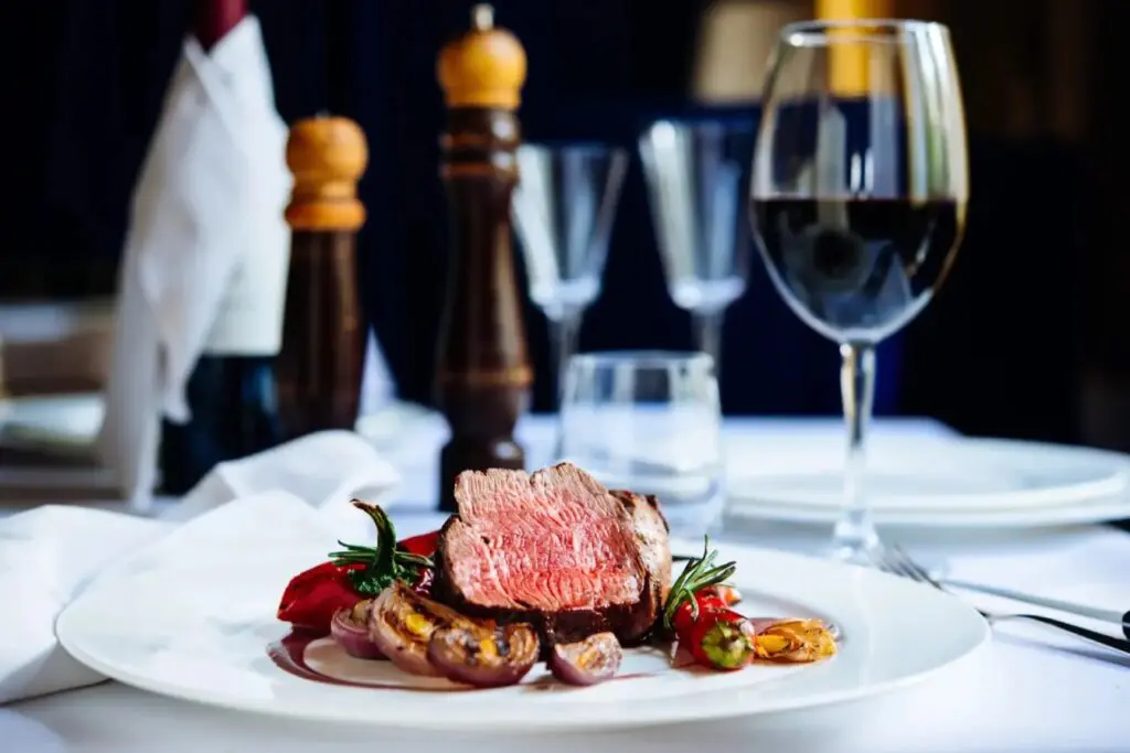 A sliced steak entree served with a glass of red wine on a set table at Brugada Kitchen & Bar