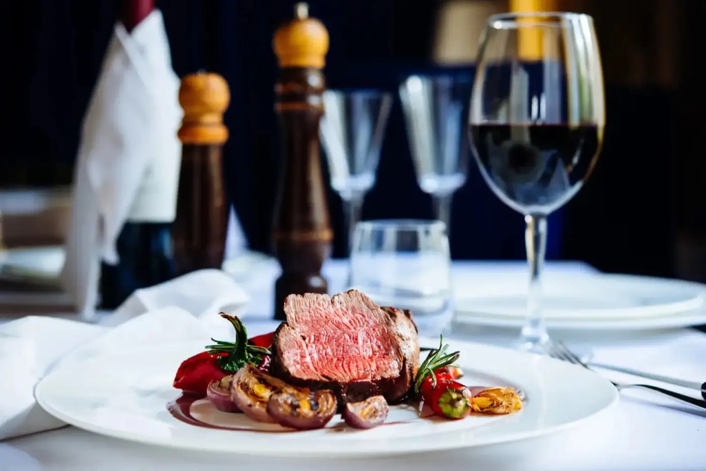 A sliced steak entree served with a glass of red wine on a set table at Brugada Kitchen & Bar