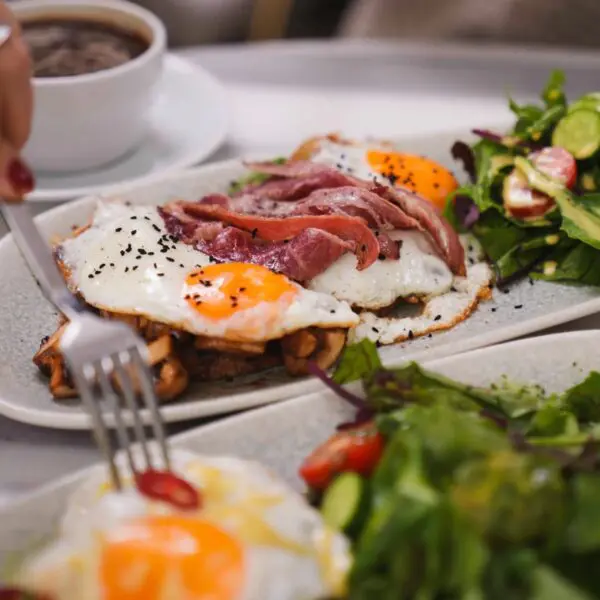 Fried eggs with crispy bacon, sauteed mushrooms and a dressed side salad, served with coffee at weekend brunch