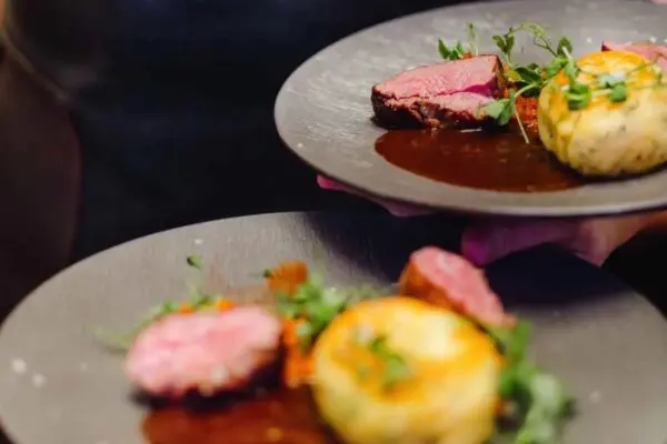 Two plated steak entrees with herbed potato and pan sauce, carried to a table at Brugada Kitchen & Bar
